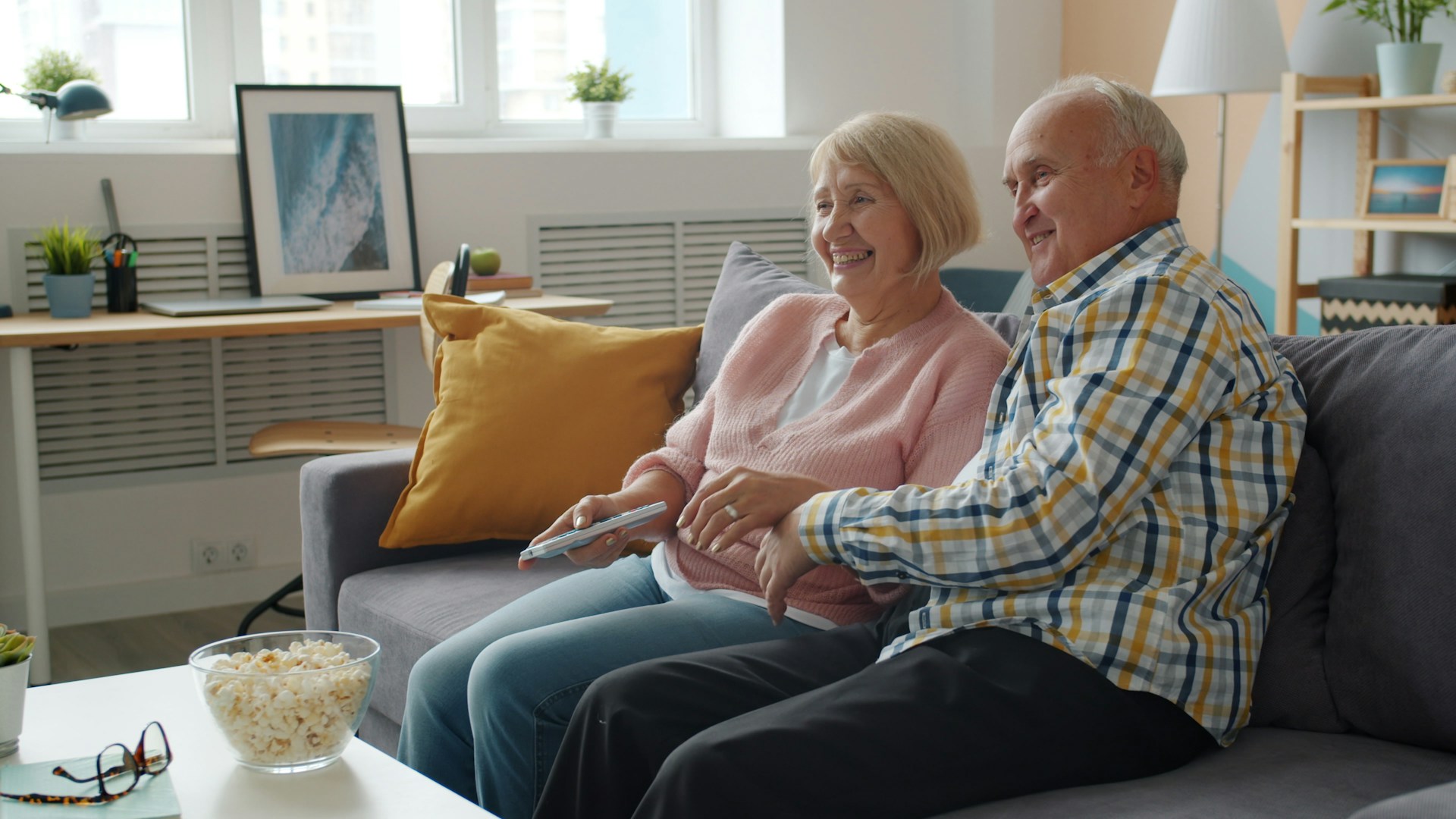 Elderly couple watching television together on sofa.