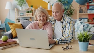 Elderly couple smiling while looking at laptop together.