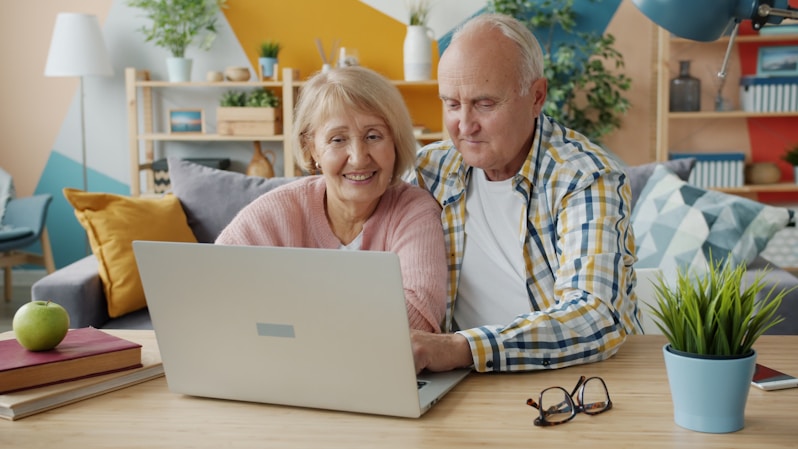 Elderly couple smiling while looking at laptop together.