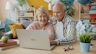 Elderly couple smiling while looking at laptop together.