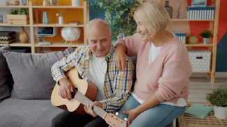 Elderly couple playing guitar together on sofa.