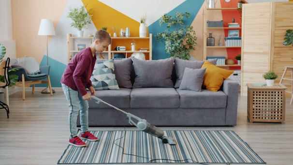 Young girl vacuuming a striped rug in a living room.