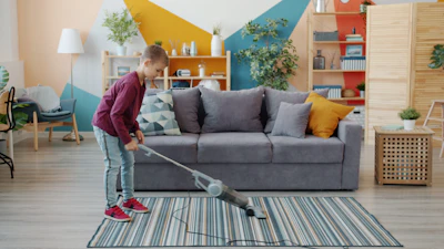 Young girl vacuuming a striped rug in a living room.