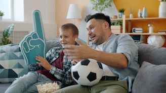 Father and son watching soccer with foam finger and popcorn.