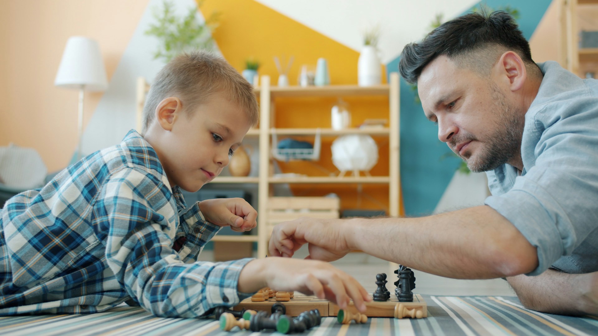 Father and son playing chess on the floor.