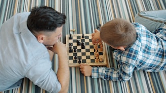 Father and son playing chess on the floor.
