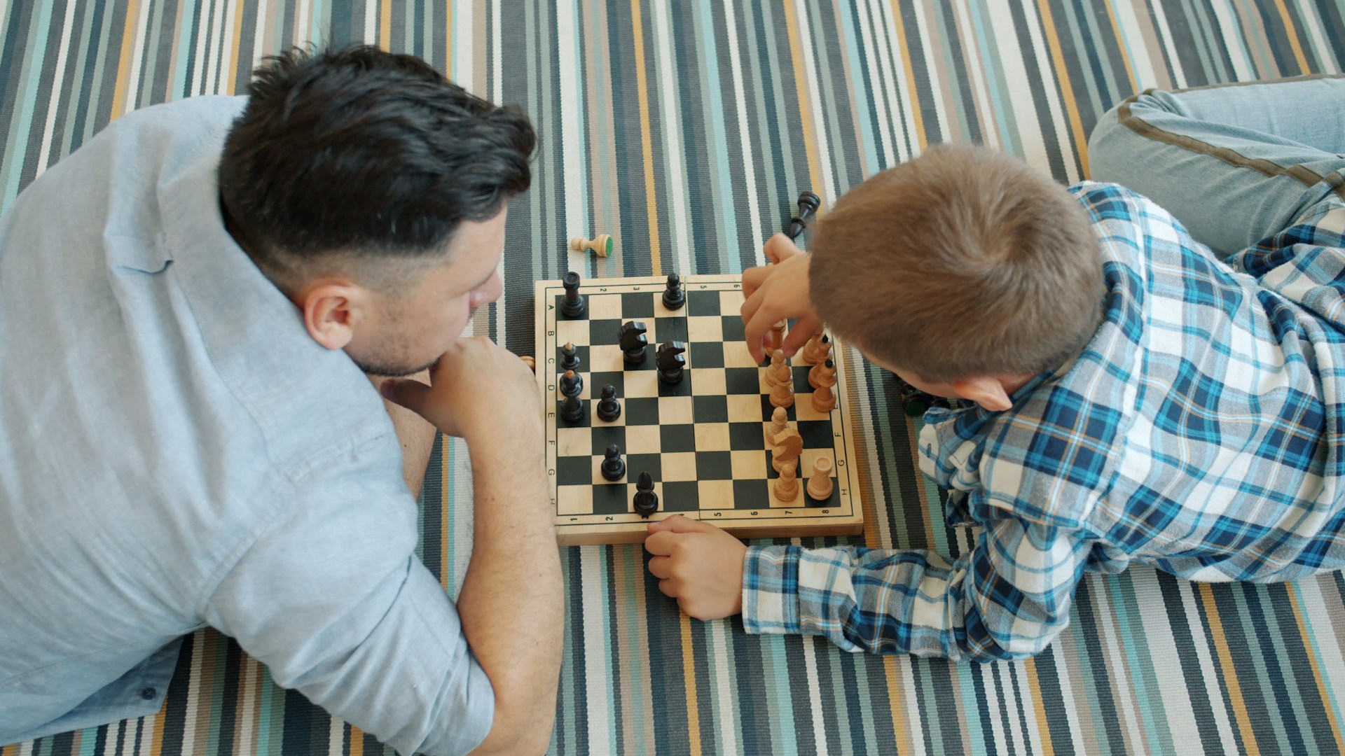 Father and son playing chess on the floor.