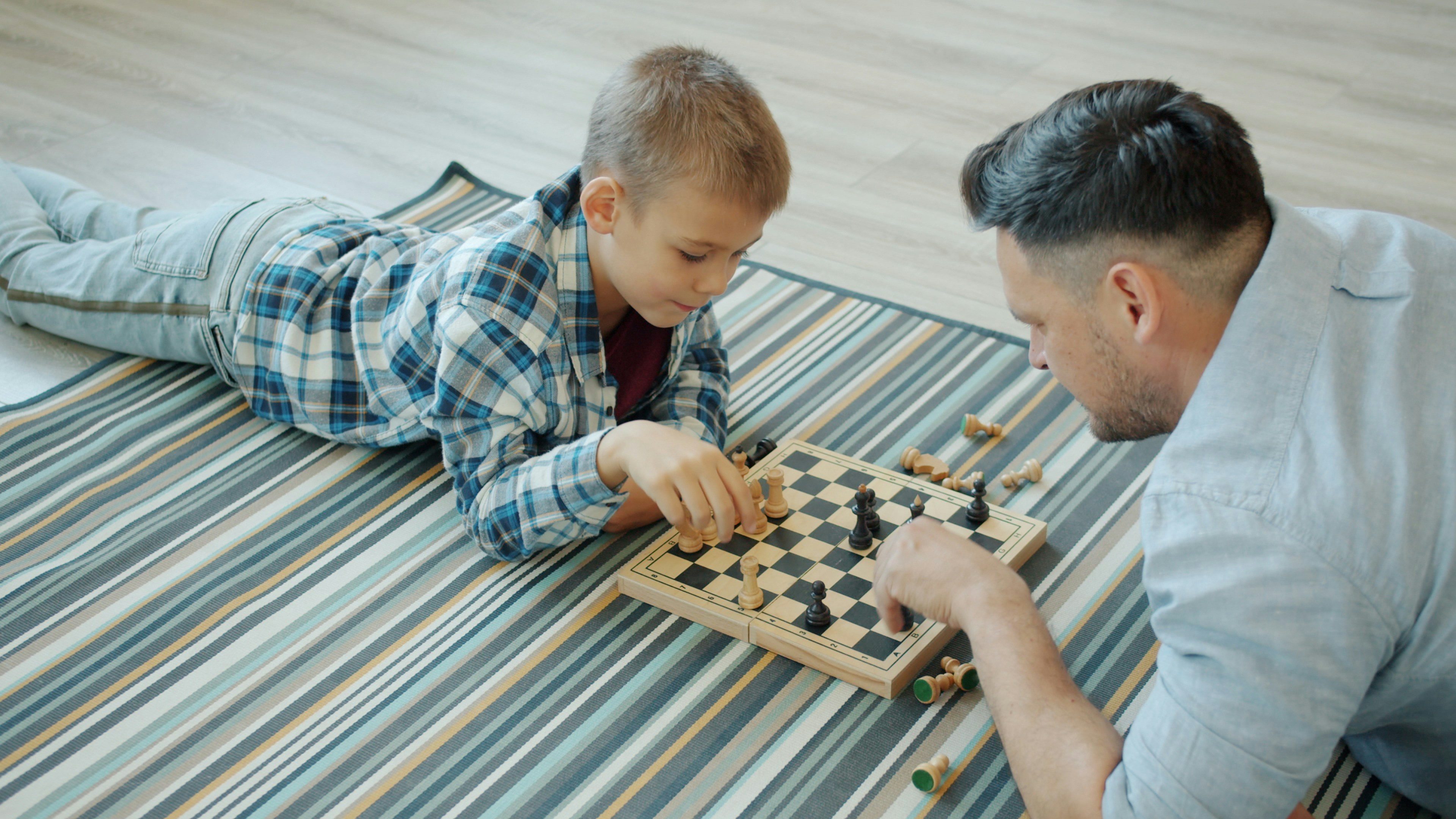 Father and son playing chess on a striped blanket.