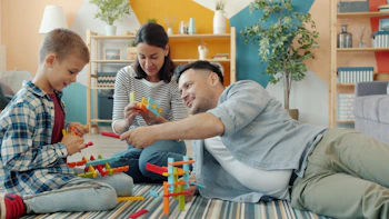 Family building with colorful toy blocks together on floor.