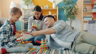 Family building with colorful toy blocks together on floor.