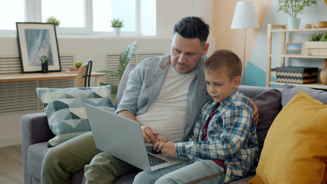 Parent proudly helping a child learn on a laptop