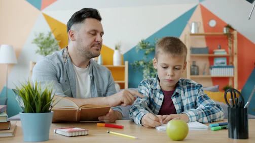 Father helping son with homework at a colorful desk.