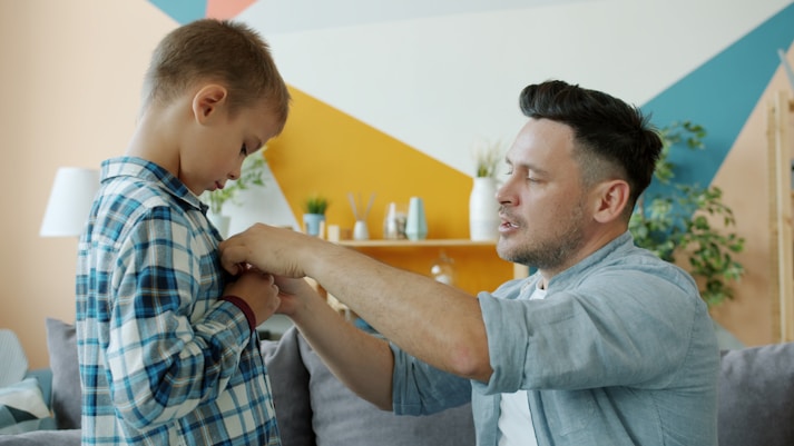 Father helps his son button his shirt.