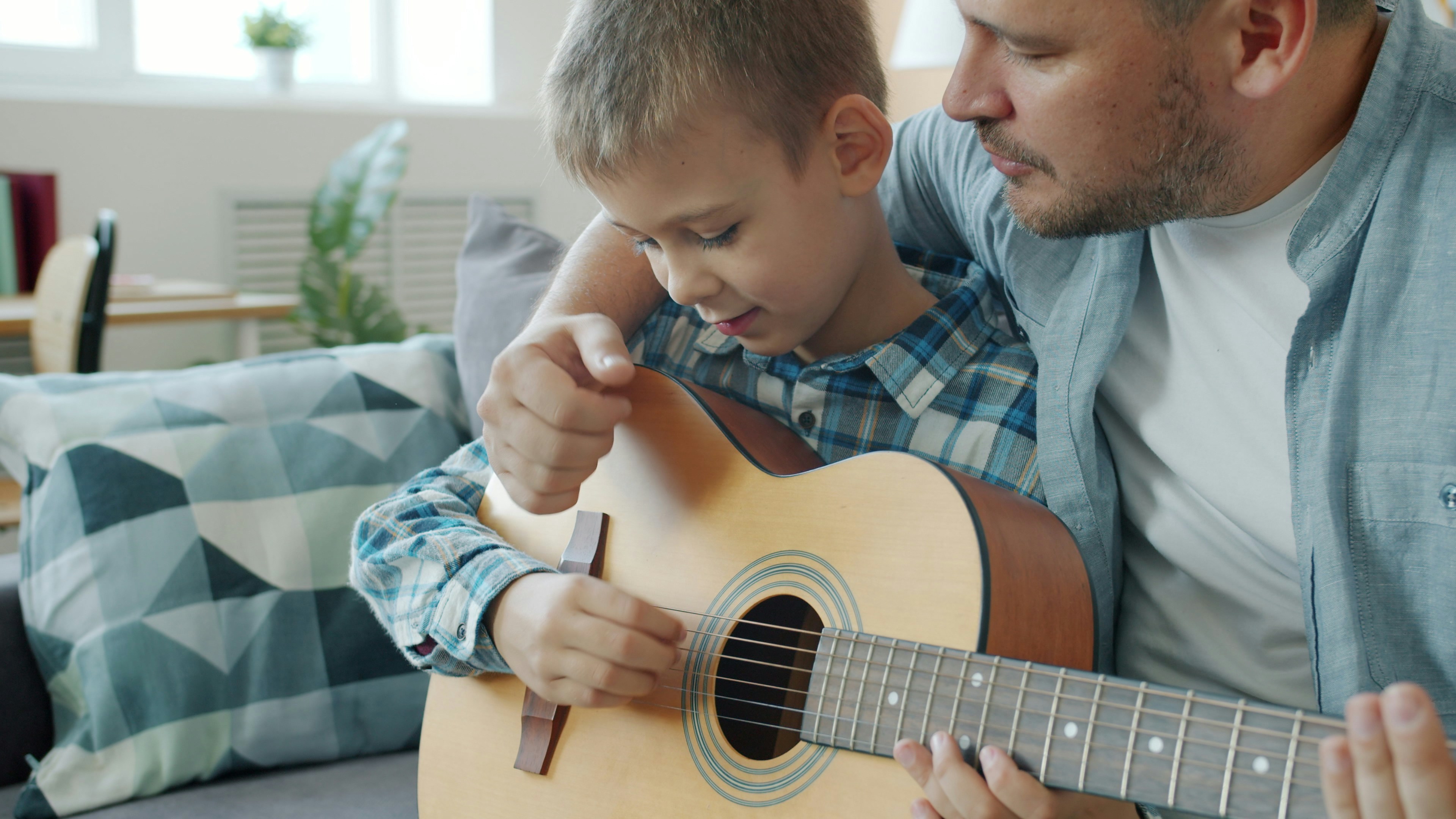 Young man is teaching little son play the guitar indoors