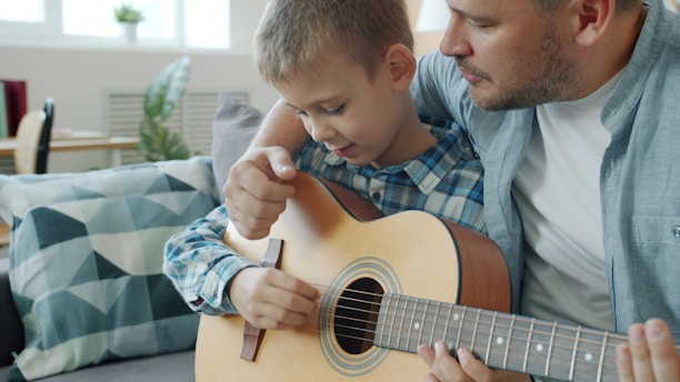 Father teaching son to play guitar at home.