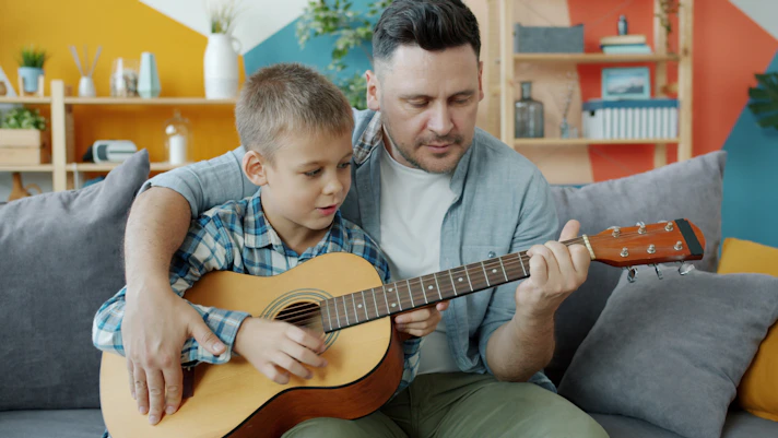 Father and son playing guitar together on sofa