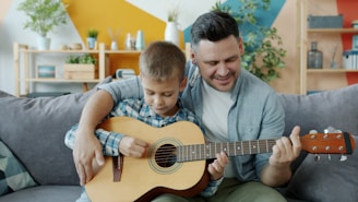 Father and son playing guitar together on couch.
