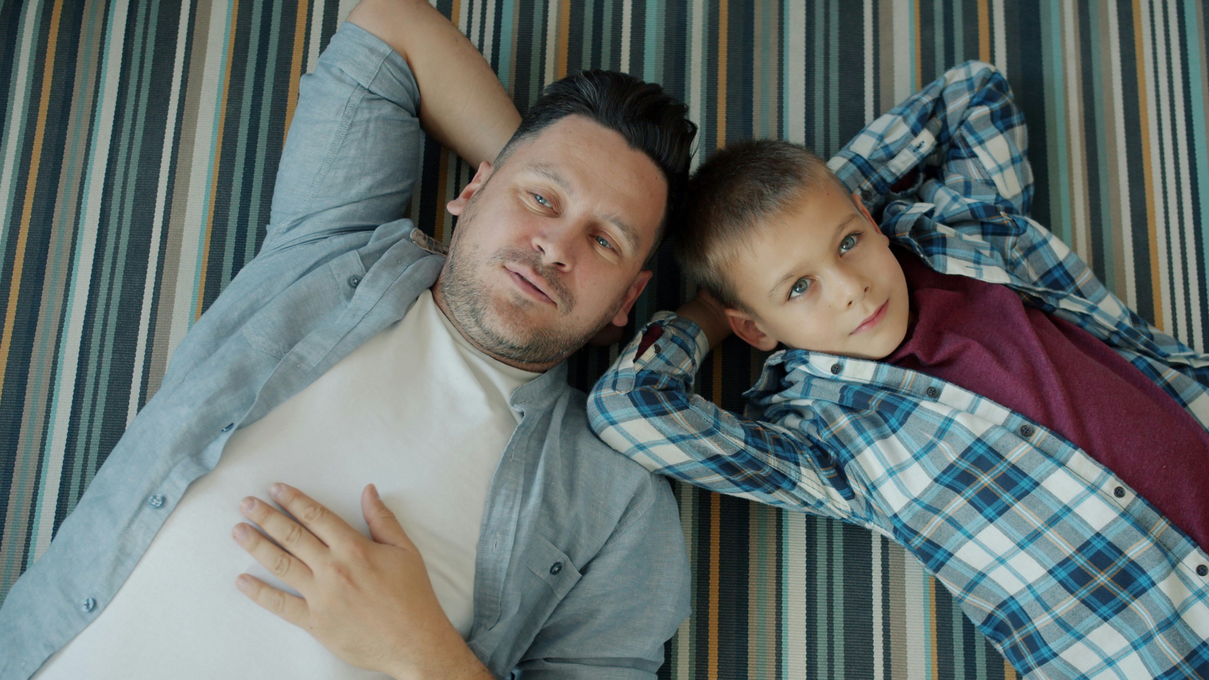 Father and son relaxing on a striped hammock.