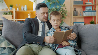 Father and son reading a book together on couch