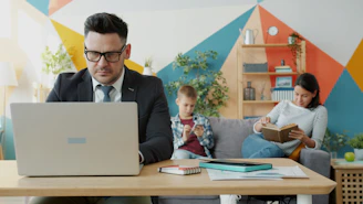 Man working on laptop while family relaxes nearby