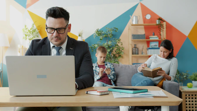 Man working on laptop while family relaxes nearby