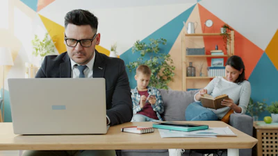 Man working on laptop while family relaxes nearby