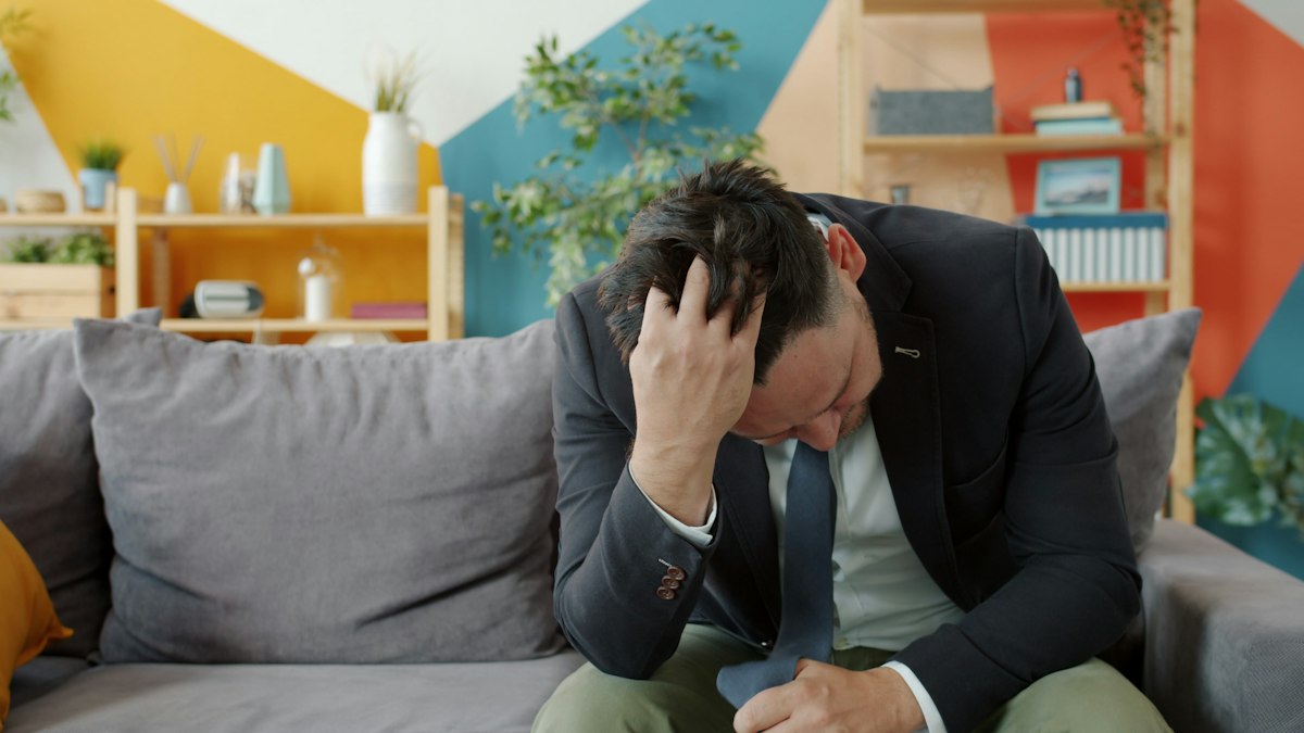 Man sitting on a couch with his head in his hands, wondering why do I feel sick after an argument