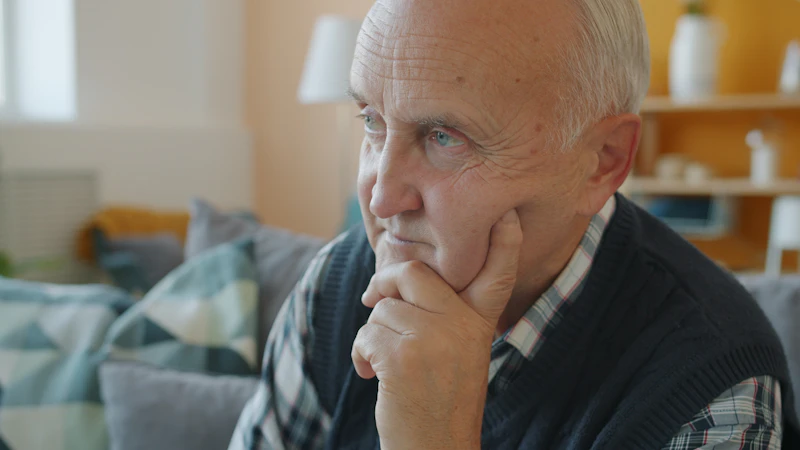 Older man sitting thoughtfully in a warm living room considering a decision