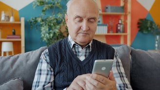 Elderly man using a smartphone on a couch.