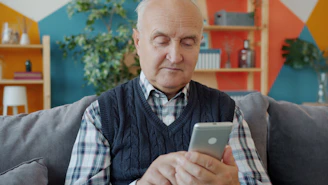 Elderly man using a smartphone on a couch.