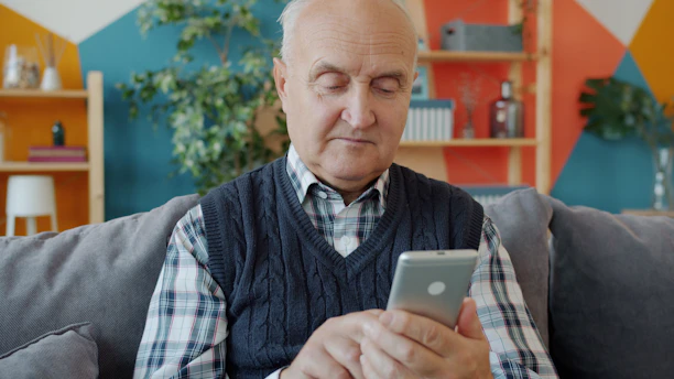 Elderly man using a smartphone on a couch.