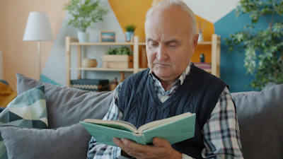 Elderly man reading a book on a couch
