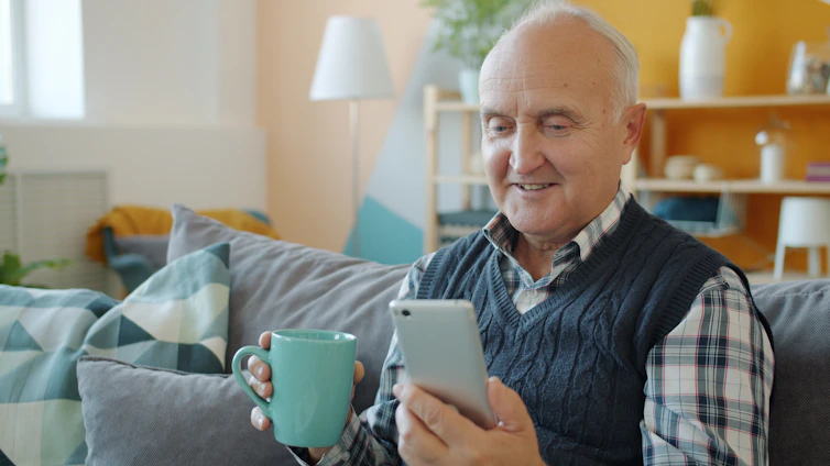 Smiling senior man holding mug and phone on couch.