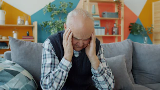 Elderly man holding head in discomfort on couch