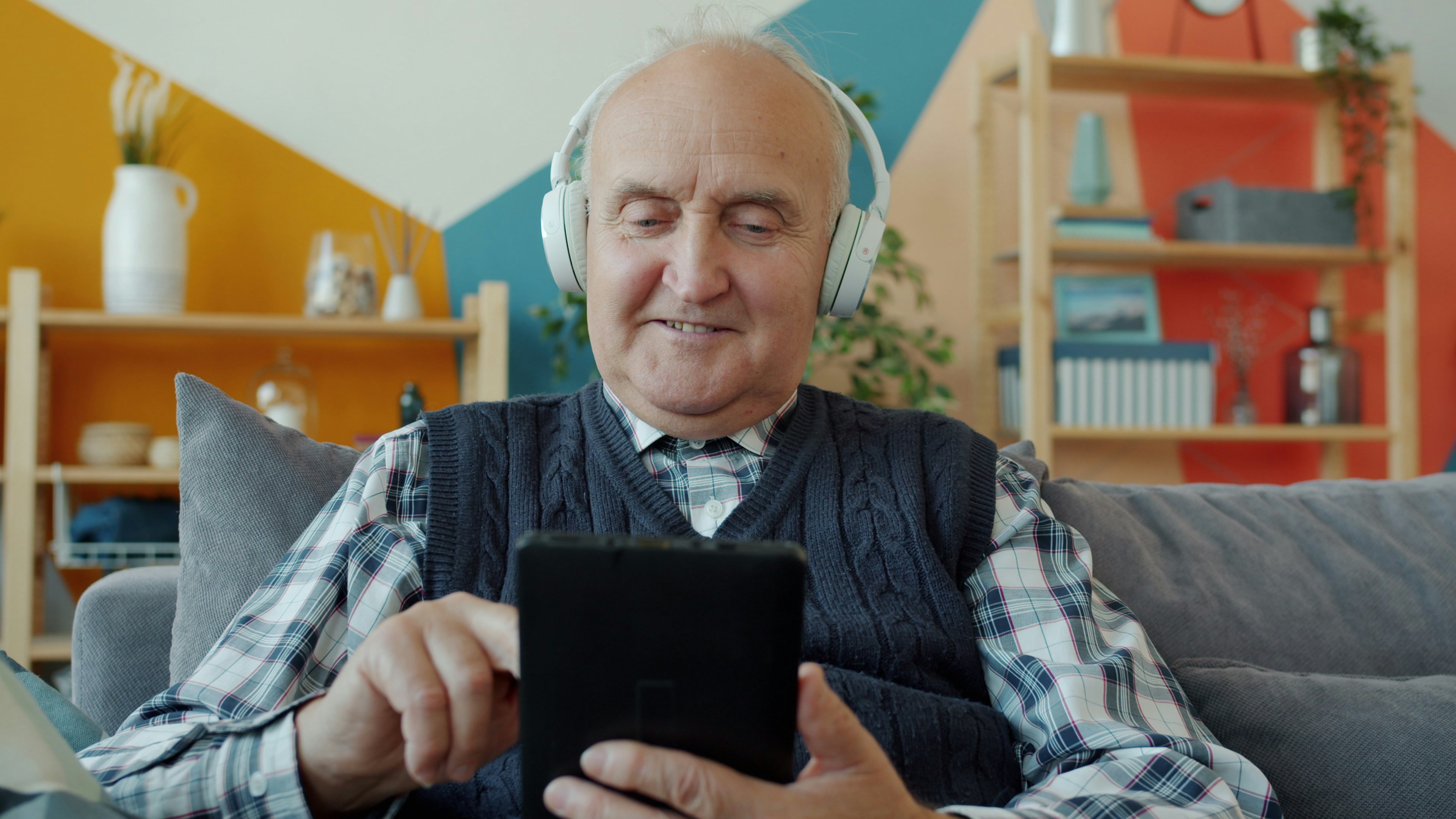 Elderly man with headphones uses a tablet.
