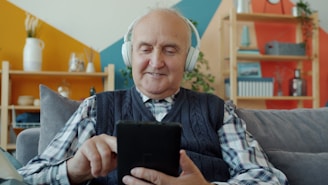 Elderly man with headphones uses a tablet.
