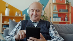 Elderly man with headphones uses a tablet.