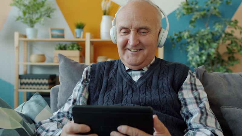 Senior man enjoying audio through headphones while using a tablet at home