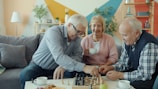 Three seniors playing chess in a living room.