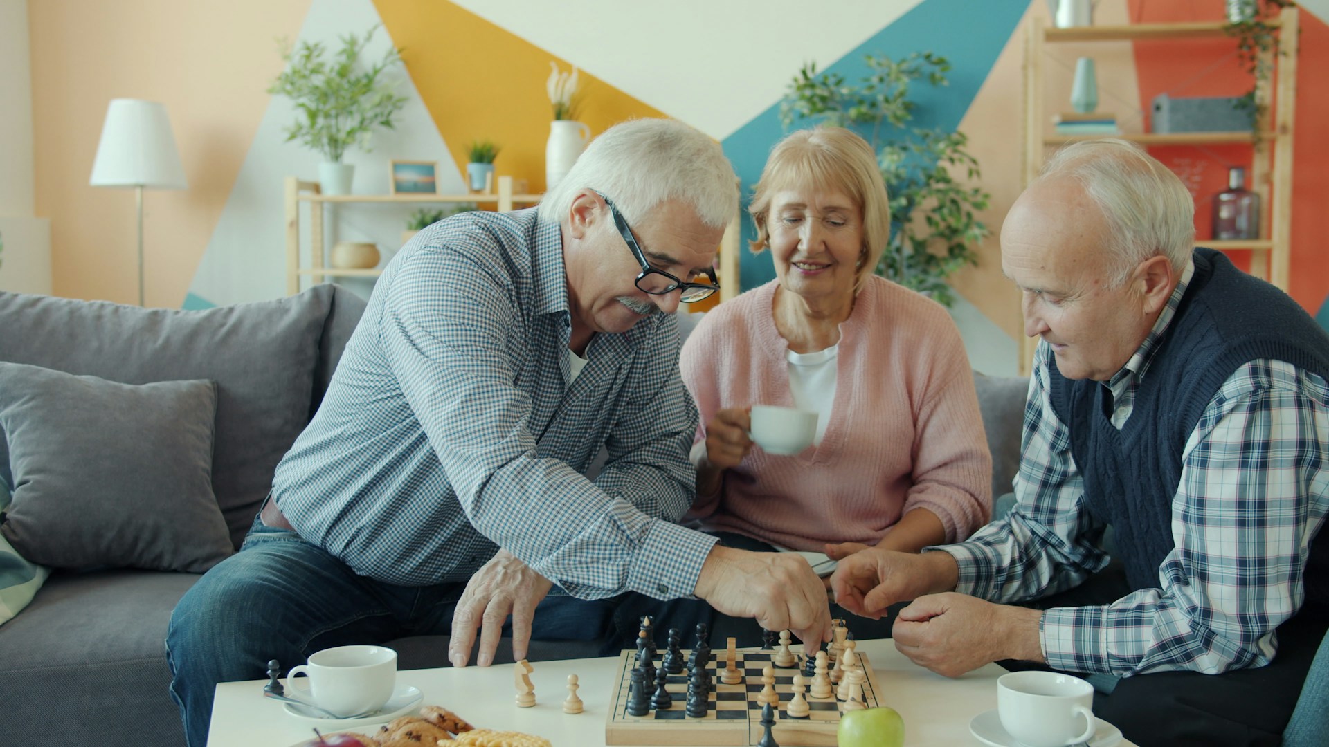 Three seniors playing chess in a living room.