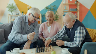 Three seniors playing chess together in a living room.