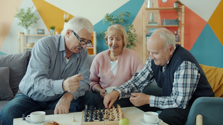 Three seniors playing chess together in a living room.