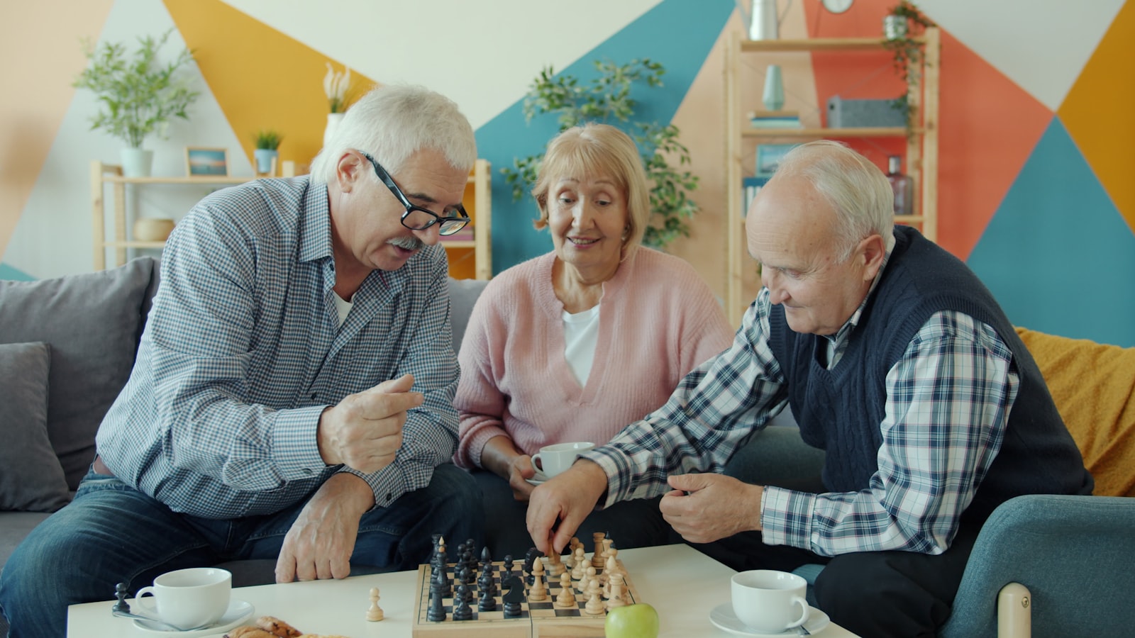 three older adults playing chess together in a living room