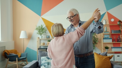 Elderly couple dancing happily in a colorful living room.