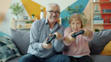 Elderly couple playing video games together on couch.