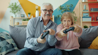 Elderly couple playing video games together on couch.