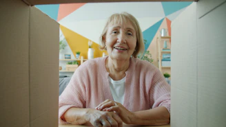 Elderly woman smiling from inside a cardboard box