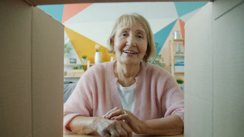 Elderly woman smiling from inside a cardboard box