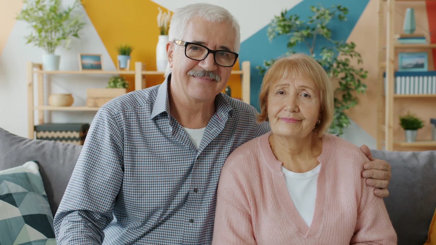 An older couple smiling together on a sofa in a bright, homely living room