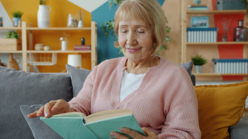 Older woman reading a book on the couch, a calm setting for memory and focus